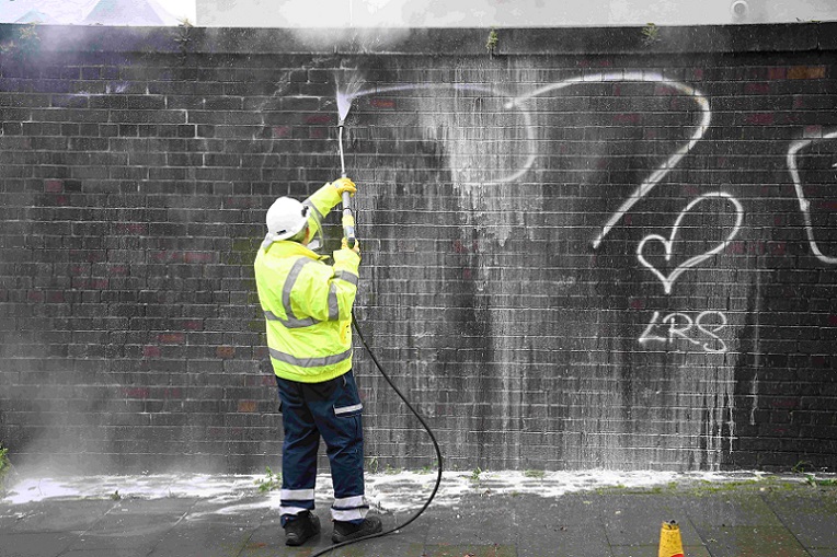 Man cleaning graffiti from a wall